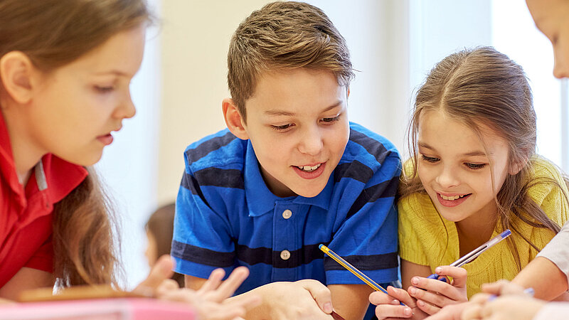 Junge Schülerinnen und Schüler, die gemeinsam etwas erarbeiten/aufschreiben