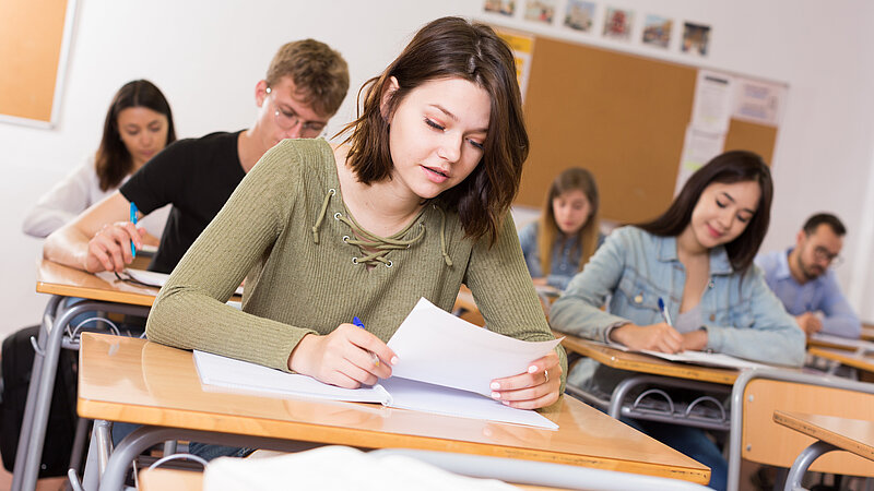 Mädchen/junge Frau schreibt Test und denkt über Fragen am Schreibtisch nach