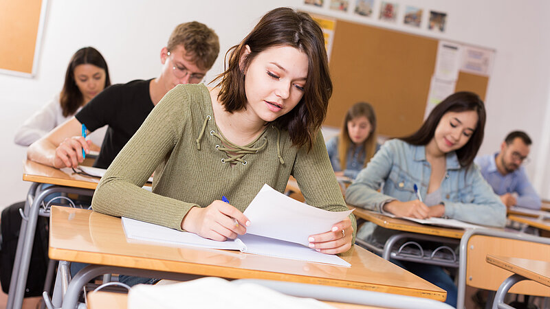 Mädchen/junge Frau schreibt Test und denkt über Fragen am Schreibtisch nach