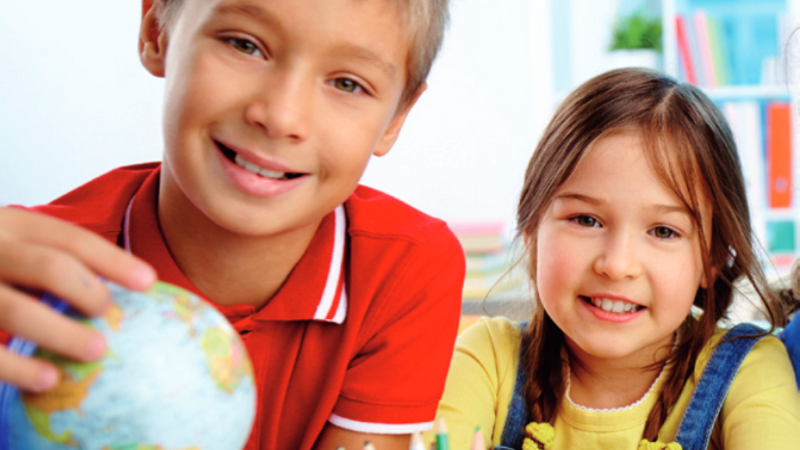 Auf dem Bild ist das Cover des bayerischen LehrplanPLUS für die Grundschule zu sehen.  Zwei Kinder sitzen an einem Tisch. Das Kind links hält einen Globus in der Hand, während das Kind rechts auf den Tisch gestützt ist. 
