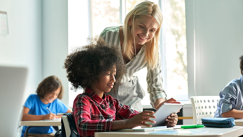 Lehrerin hilft einem Schulmädchen bei Übungen am Tablet