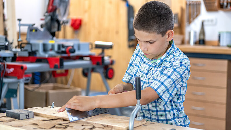Junge schneidet Holzbretter an einer Werkbank
